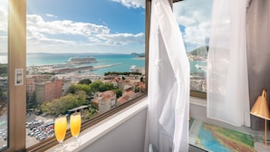 Una habitación con un amplio ventanal que ofrece vistas a una ciudad costera, incluyendo un crucero y el puerto.