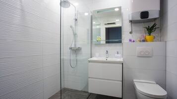 Un baño moderno con ducha de vidrio, un lavamanos blanco y un inodoro.