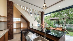 A modern kitchen with a large island, a built-in sink, and a view of a garden through a large window. - Liam Private Villa (Sukawati)