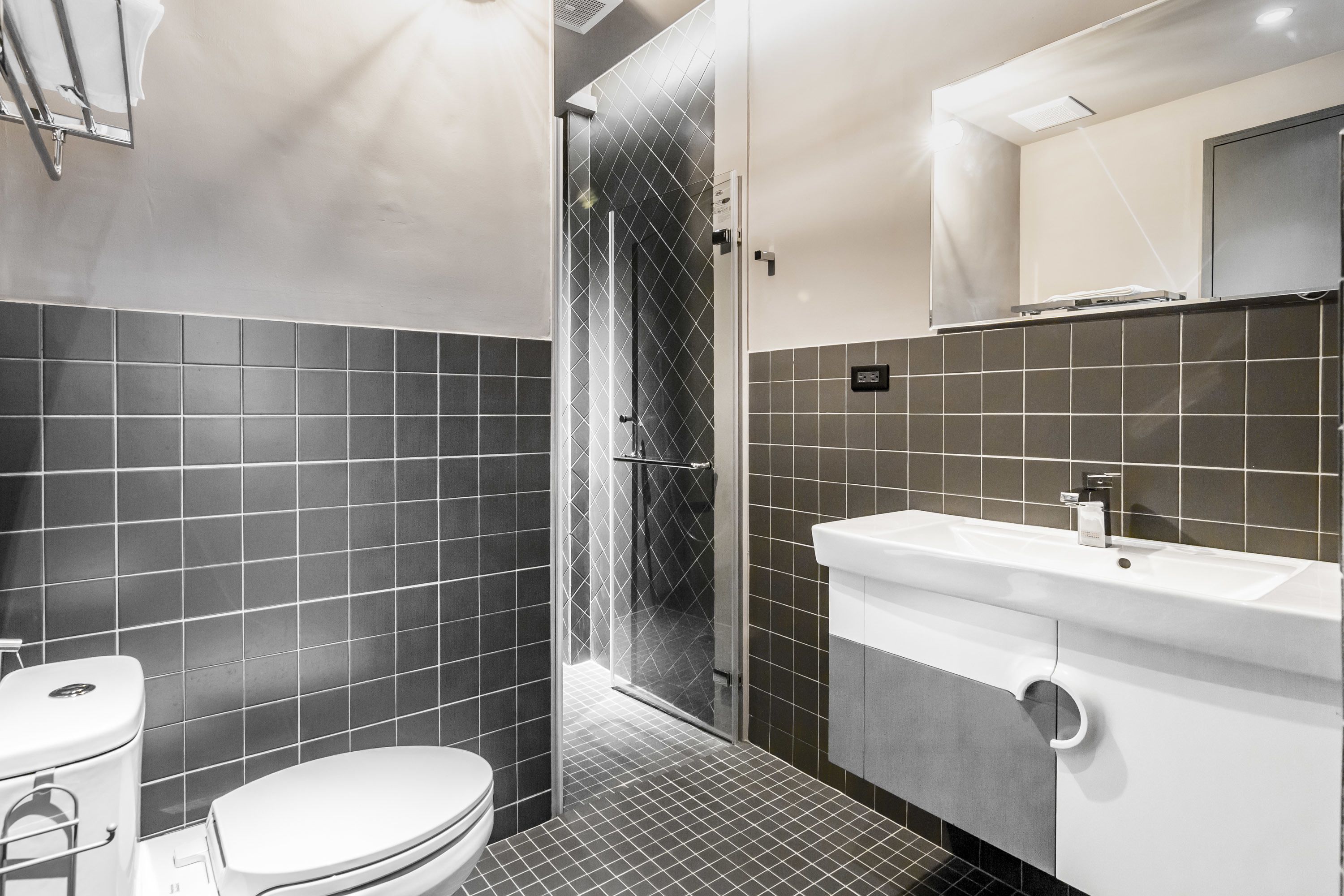 A modern bathroom with a toilet, a shower enclosure, and a sink with a mirror above it.