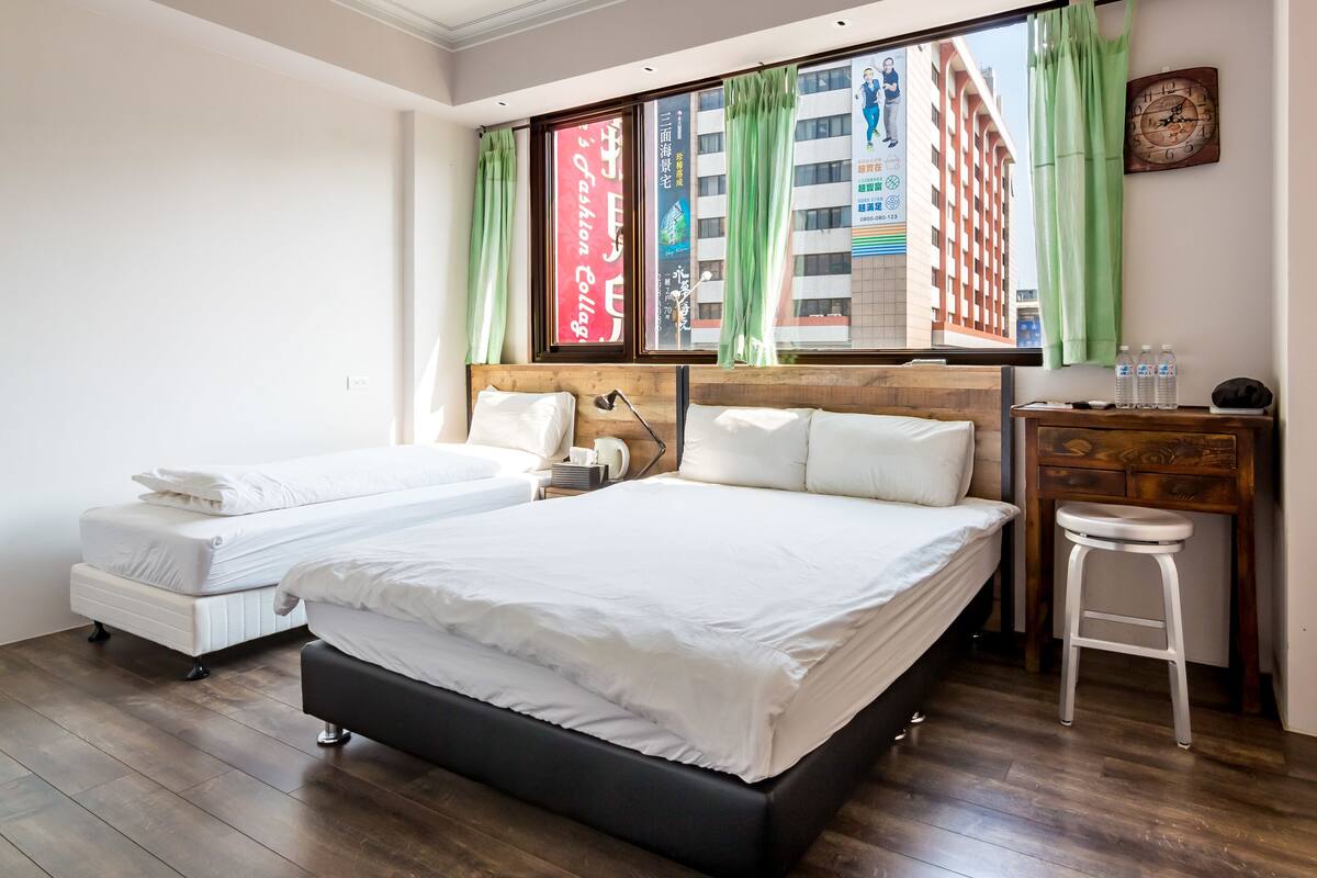 Een hotelkamer met twee bedden, een houten bureau, een stoel en een raam met gordijnen.