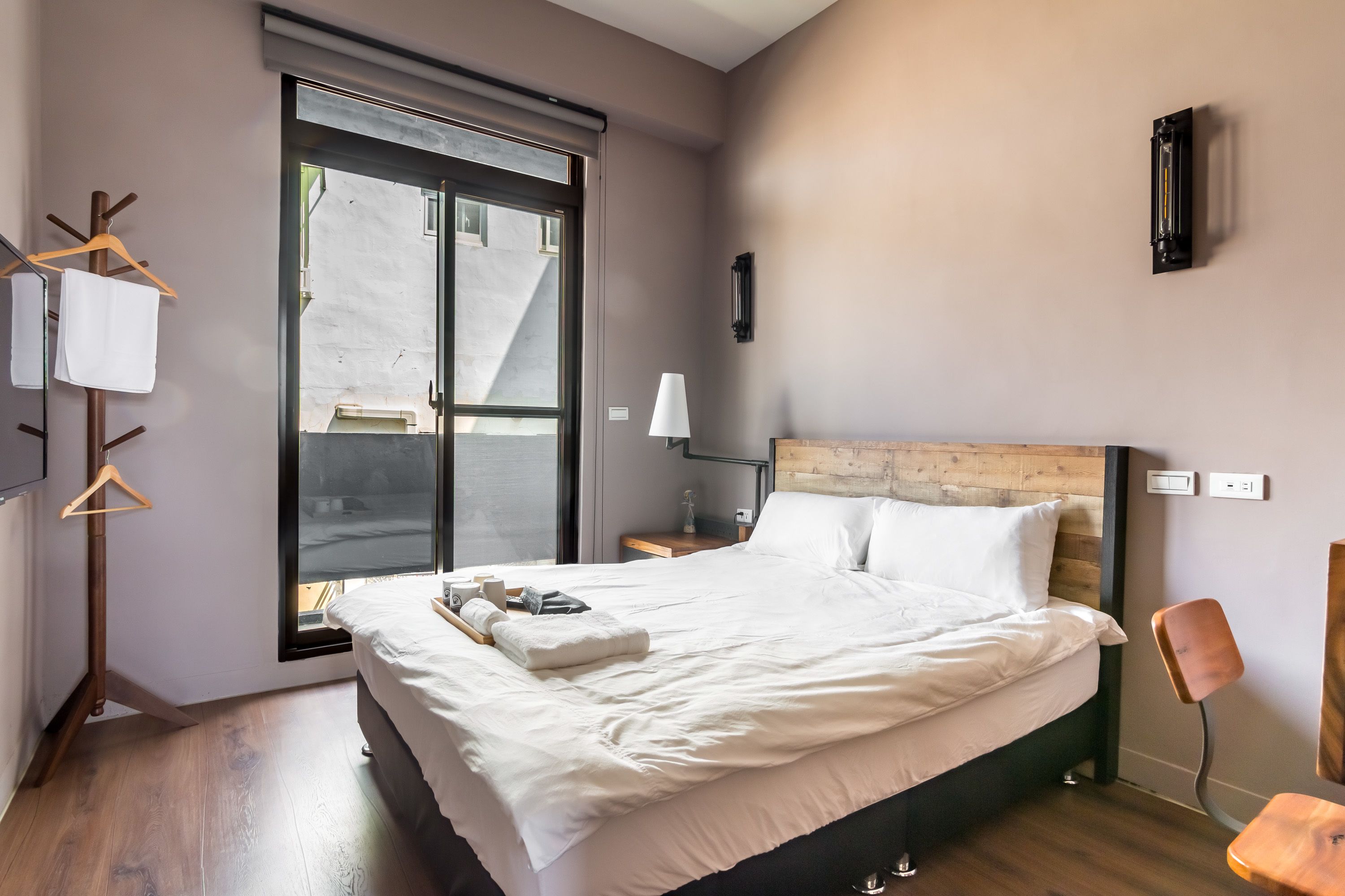 Ein modernes Schlafzimmer mit einem großen Bett, Holzboden, einem Fenster und einer Wandlampe.