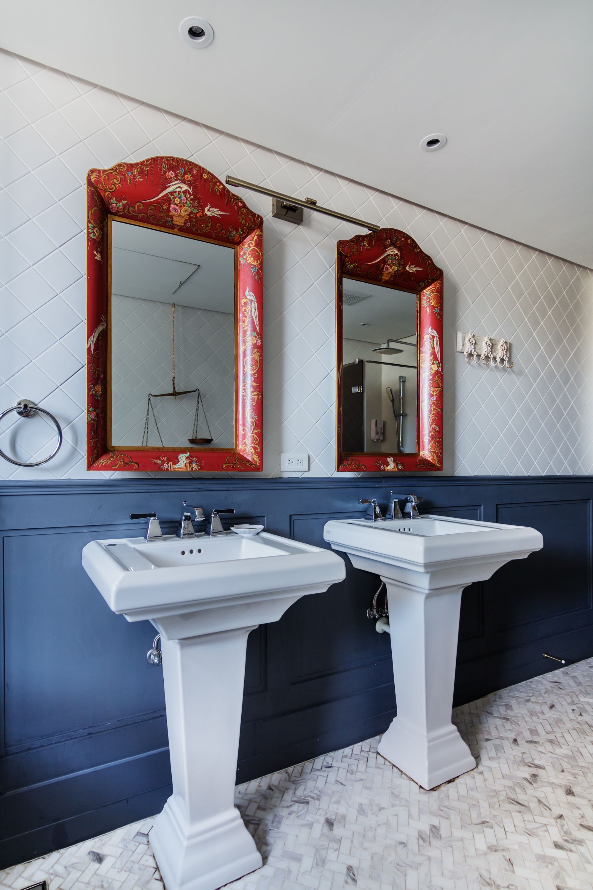 Une salle de bain avec deux lavabos blancs, un miroir à cadre rouge et un mur bleu.
