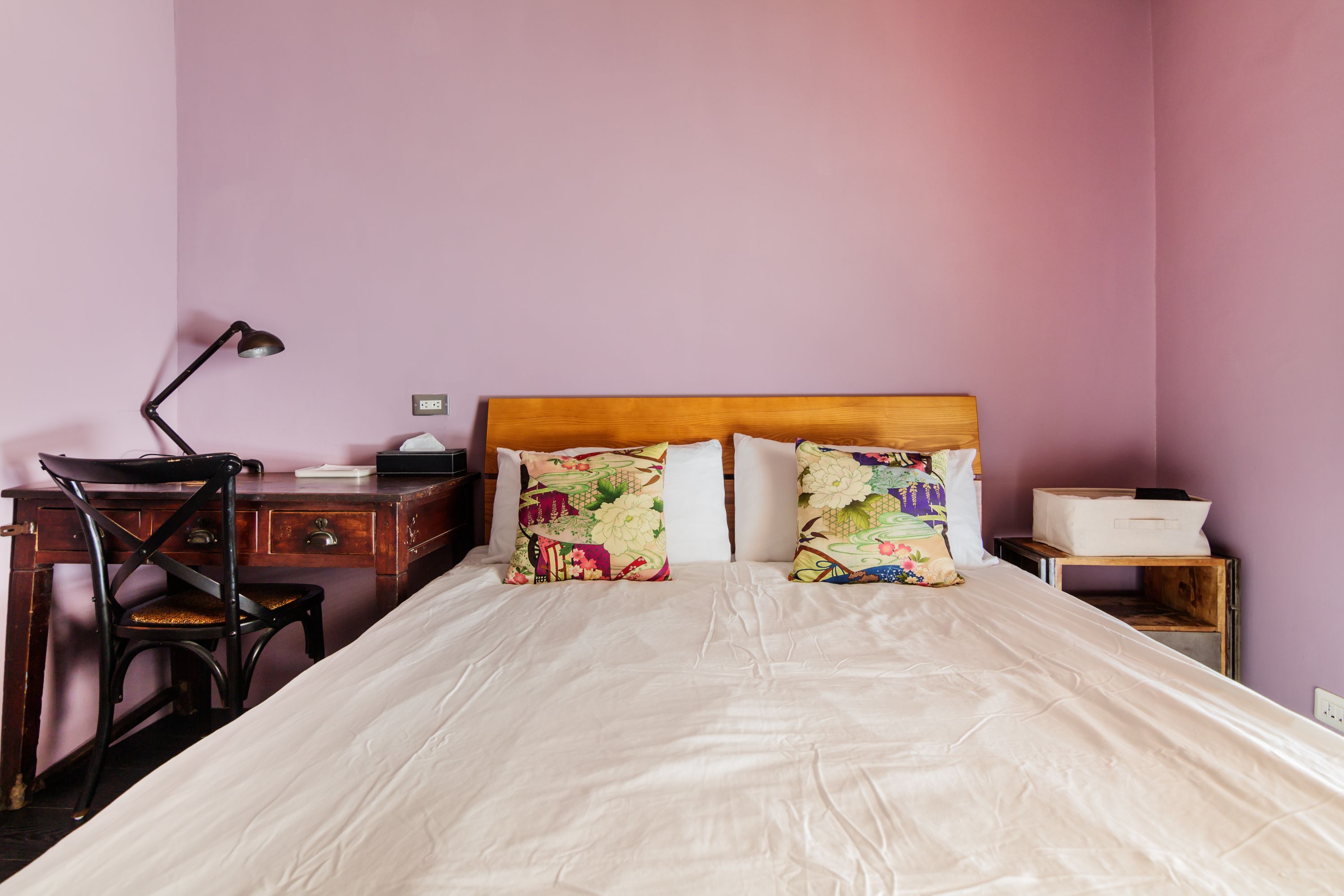 A bedroom with a wooden headboard, a desk with a chair, and a bedside table with a lamp.