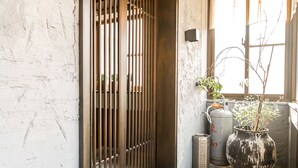 Um corredor com parede de mármore, portão de metal, planta em vaso e janela com luz natural.
