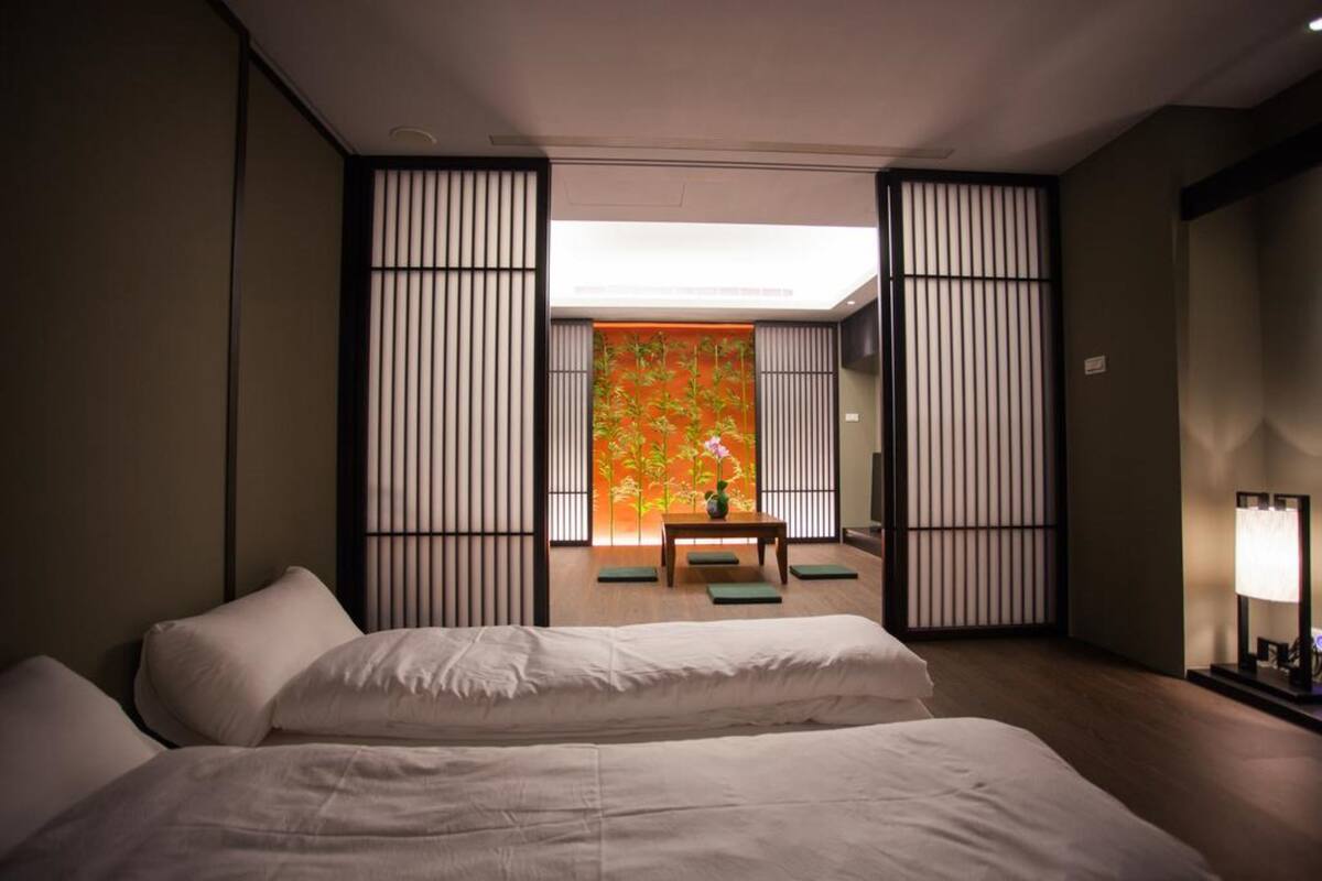 Een hotelkamer met twee bedden, een klein tafeltje met een vaas en uitzicht op een traditionele Japanse kamer door een schuifdeur.