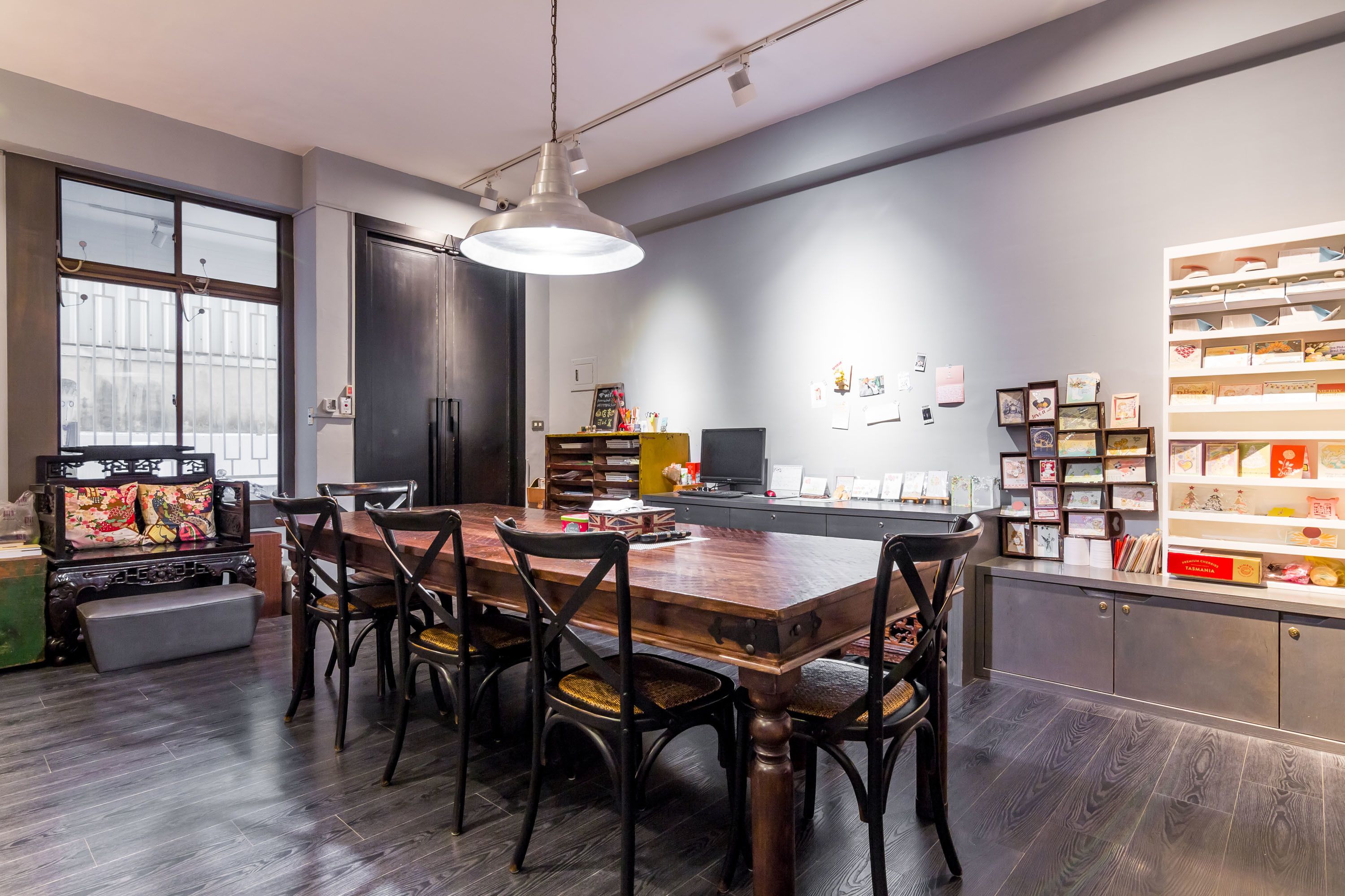 A modern kitchen with a wooden dining table, dark wood flooring, and a large window.