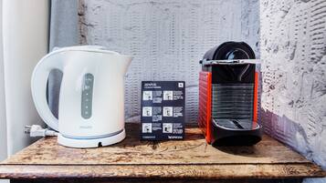 A white Philips kettle, a black and red Nespresso machine, and a user manual on a wooden surface against a textured wall.