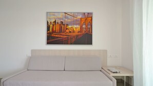 A hotel room with a bed, a desk, and a large cityscape painting on the wall. - Appartamenti Mare (Lignano Sabbiadoro)