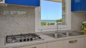 A kitchen with granite countertops, a gas stove, a double sink, and a window offering a view of the sea. - Appartamenti Mare (Lignano Sabbiadoro)