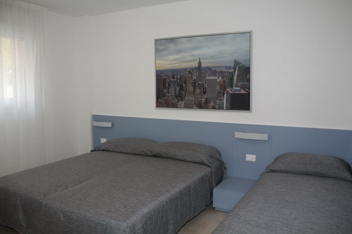 A hotel room with two single beds, a cityscape painting on the wall, and a window with curtains.