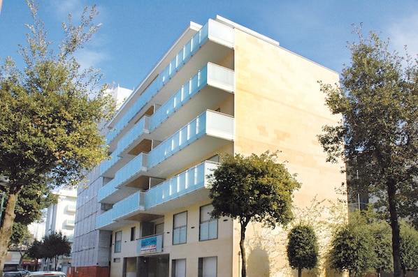 A multi-story building with balconies, a sign indicating a business or office space, and trees in the foreground.