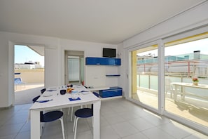 A modern dining area with a white table and blue chairs, a blue cabinet, and a sliding glass door leading to an outdoor balcony with a view of buildings.