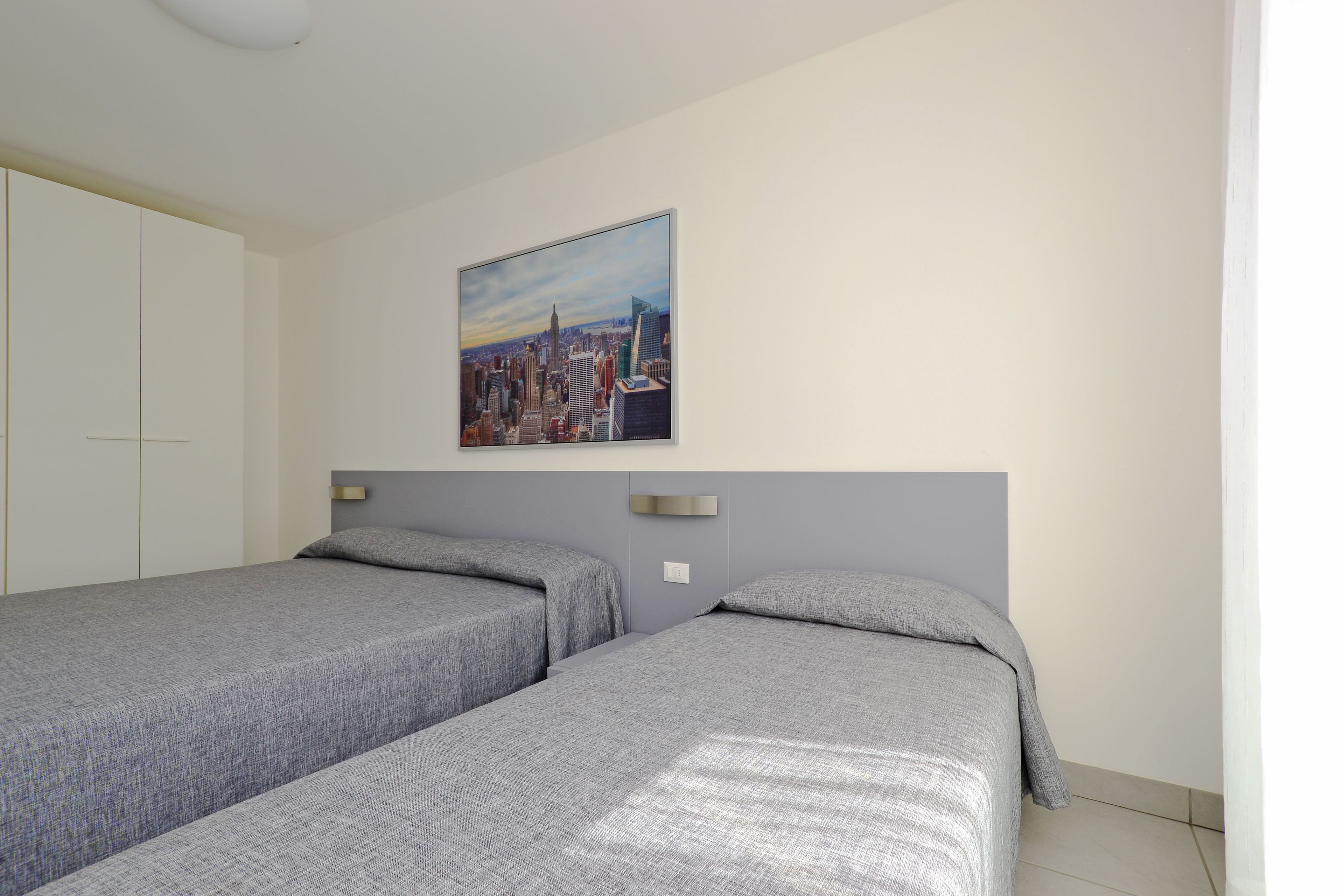 Ein Schlafzimmer mit zwei Einzelbetten, einem Stadtbild an der Wand und einem weißen Kleiderschrank.