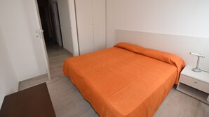 A bedroom with a bed, a nightstand, a wardrobe, and a door leading to another room.