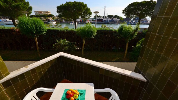 A balcony with a tiled wall, a table with a fruit bowl, and a view of a marina with boats and trees.