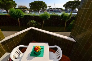 En balkon med flisevæg, et bord med en skål frugt og udsigt til en lysthavn med både og træer.