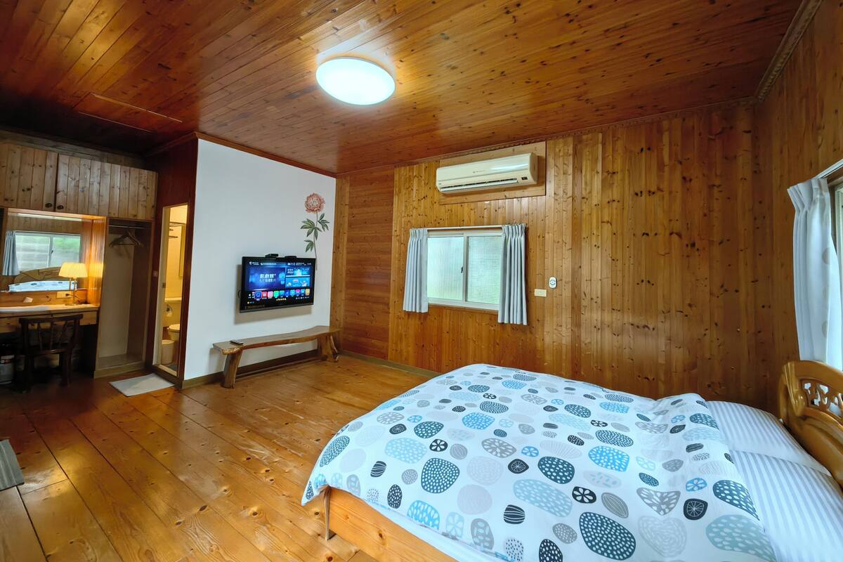 A wooden-paneled room with a bed, a TV mounted on the wall, and a bench.