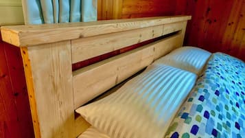 Ein Bett mit Holzkopfteil, ein Fenster mit Vorhängen und eine gestreifte Bettdecke.