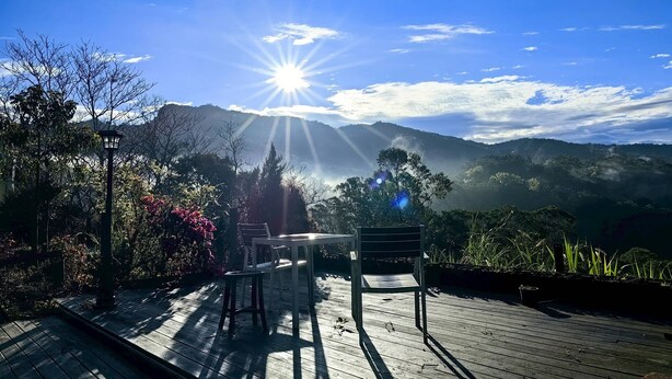 A wooden deck with chairs and a table, overlooking a mountainous landscape under a clear sky. - Fong Chou Cottage (Sanyi)