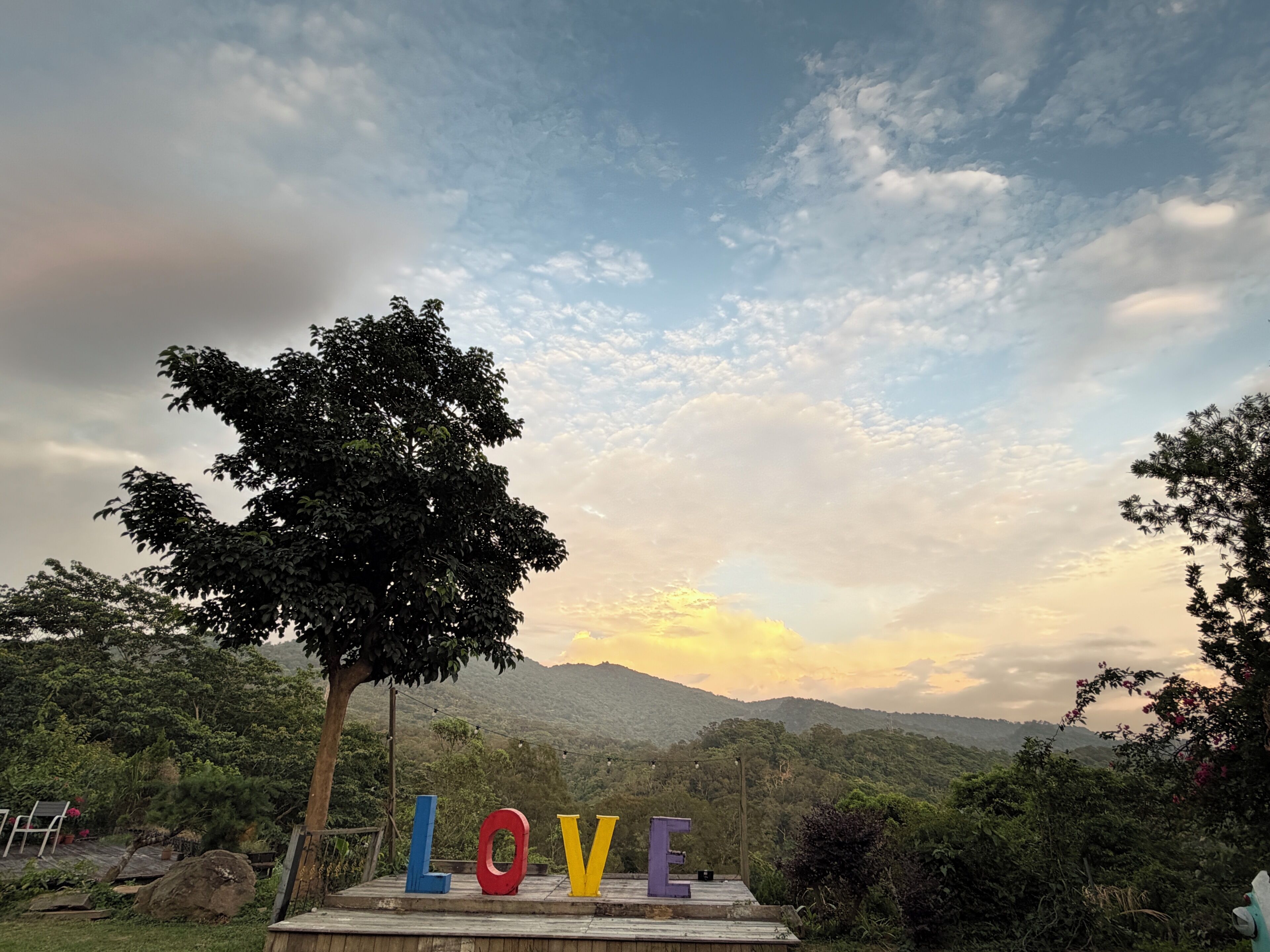 A scenic outdoor area with a wooden platform displaying the word 'LOVE' in colorful letters, surrounded by lush greenery and mountains in the background.