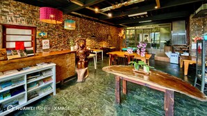 A restaurant interior with brick walls, wooden ceiling beams, and a marble floor. There are tables and chairs, a counter with a menu, and decorative elements like a star ornament and potted plants. - Fong Chou Cottage (Sanyi)