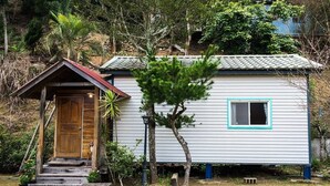 A small, single-story house with a wooden door and steps leading up to a porch. - Fong Chou Cottage (Sanyi)