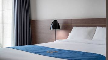 Una habitación de hotel con cama, lámpara de noche y ventana con cortinas.