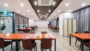 A conference room with multiple tables and chairs, a partition wall, and a door with a sign. - Golden Tulip Essential Namgang (Jinju)