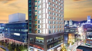 A multi-story hotel with a modern design, featuring a prominent corner location, a ground-level retail space, and a parking area. - Golden Tulip Essential Namgang (Jinju)