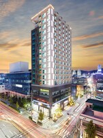 Un hotel de varios pisos con diseño moderno, ubicado en una esquina destacada, con espacio comercial en la planta baja y una zona de estacionamiento.