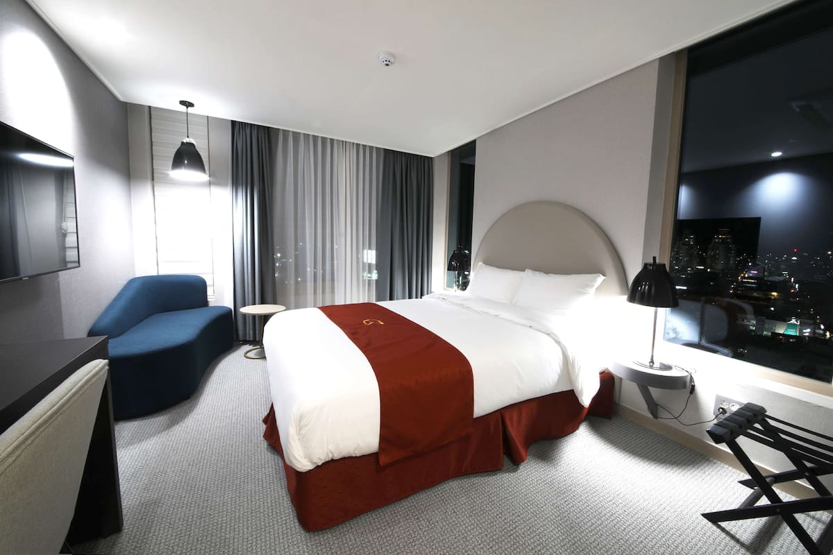 Een hotelkamer met een groot bed, een bureau, een stoel, uitzicht over de stad en een raam met gordijnen.