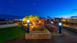 An outdoor terrace with a view of the city skyline at dusk, featuring a brick planter with plants and seating areas. - Golden Tulip Essential Namgang (Jinju)