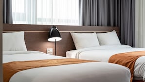 A hotel room with two beds, a nightstand, a lamp, and a window with curtains. - Golden Tulip Essential Namgang (Jinju)