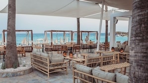 An outdoor seating area with wicker furniture and tables, overlooking the sea. - Nissi Beach Resort (Ayia Napa)