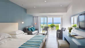 A hotel room with two beds, a sofa, a desk, and a balcony with a view of the ocean. - Nissi Beach Resort (Ayia Napa)