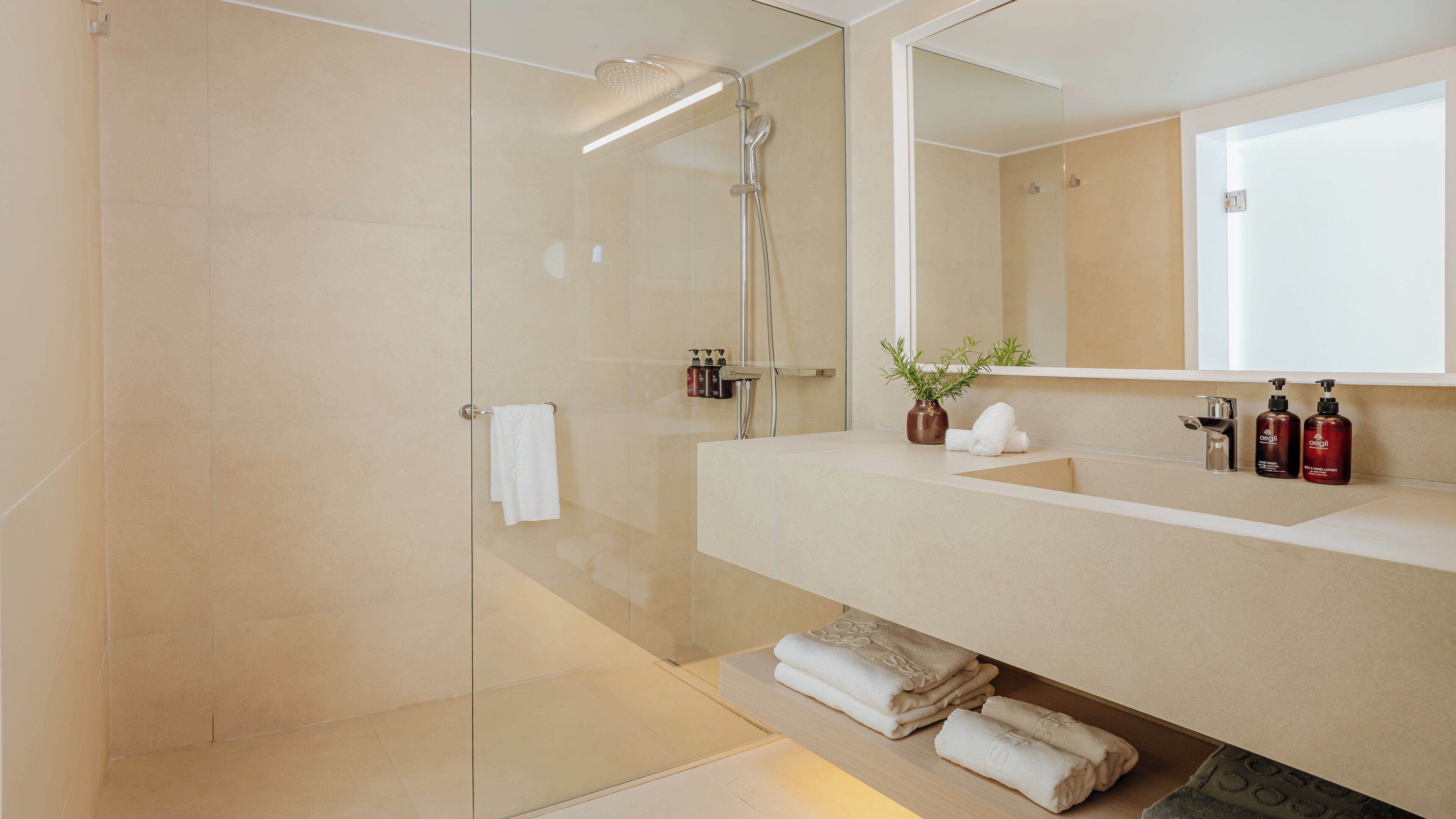 A modern bathroom with a glass shower enclosure, a vanity with a mirror, and neatly folded towels.