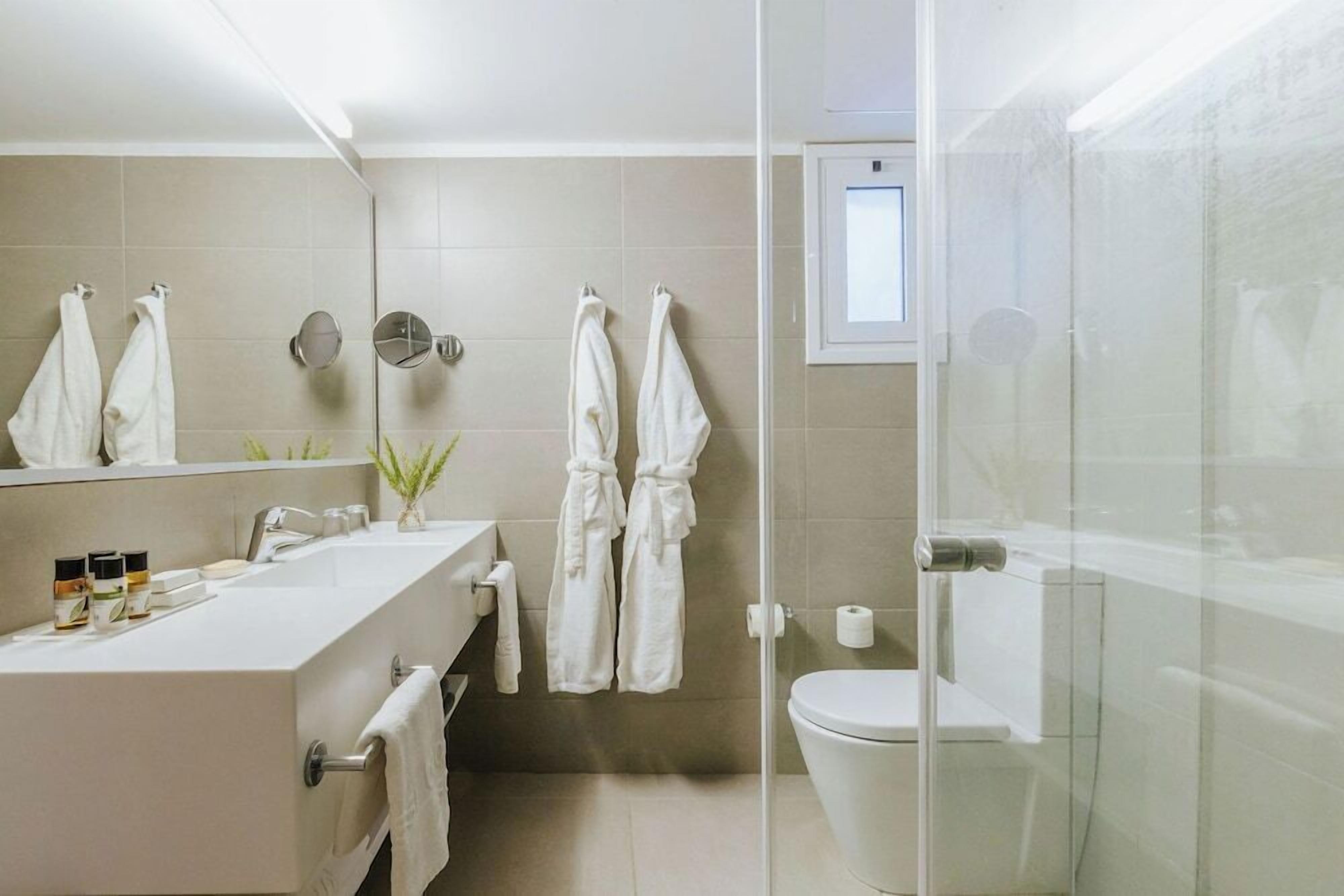 A modern bathroom with a glass shower enclosure, a white sink with toiletries, and two towels hanging on the wall.