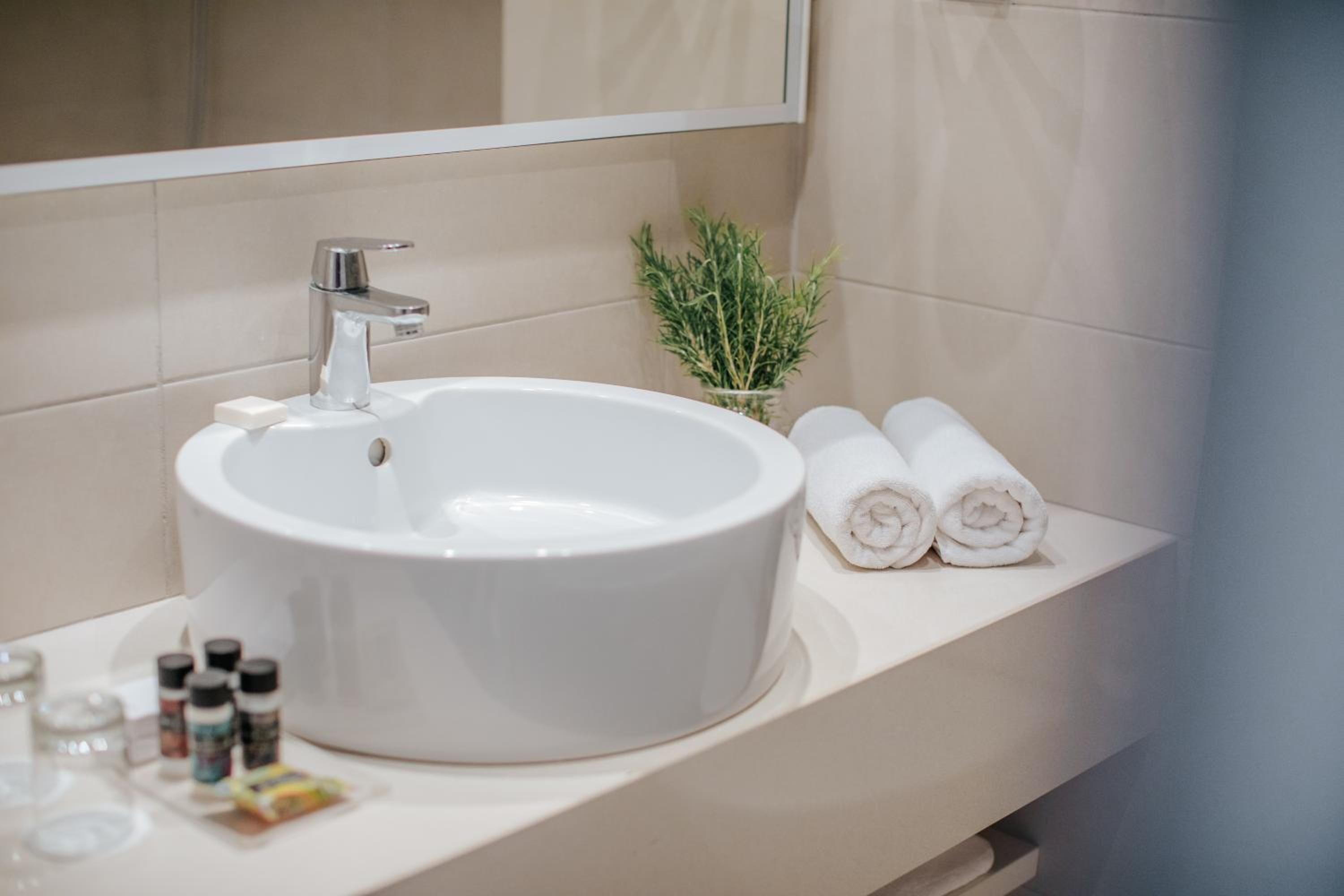 Un bagno con un lavandino bianco, uno specchio e uno scaffale con asciugamani arrotolati.