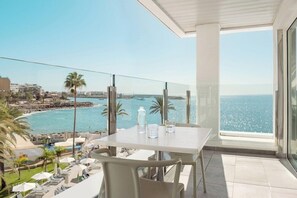 A balcony with a table and chairs, overlooking a beach and ocean. - Sunwing Arguineguin (Mogan)