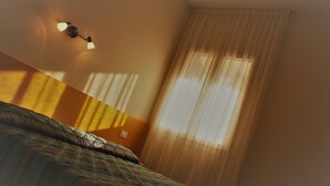 Hotellihuone, jossa on sänky, seinään kiinnitetty valaisin ja ikkuna, jossa on verhot.
