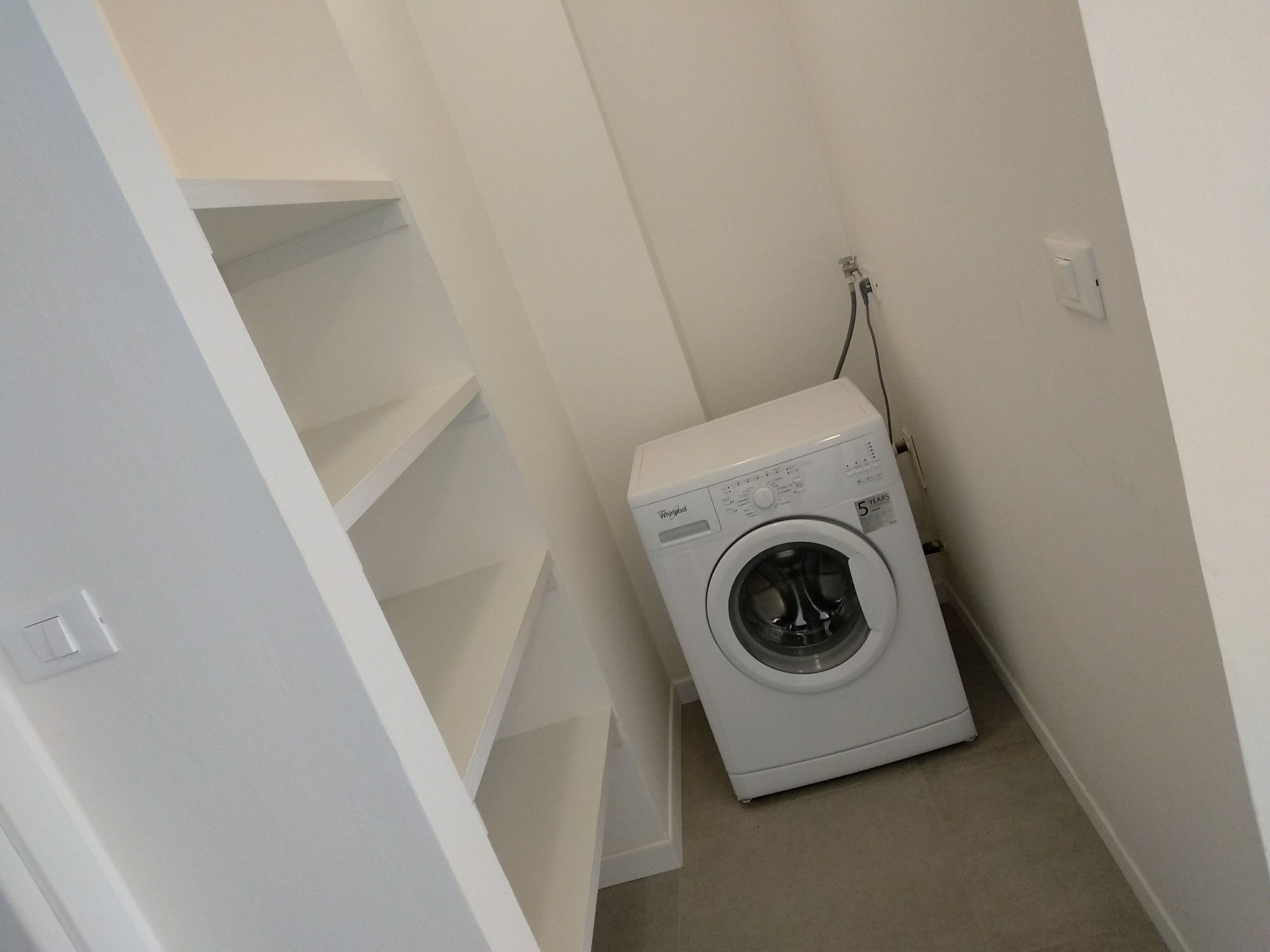 Une petite buanderie équipée d’un lave-linge et d’un sèche-linge à chargement frontal, d’un mur blanc et d’un sol carrelé.
