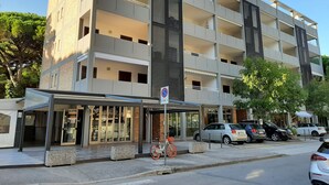 Moderni, useita kerroksia sisältävä rakennus, jossa on katettu sisäänkäynti, ulkotila istumiseen ja pyörä, joka on pysäköity ulos.