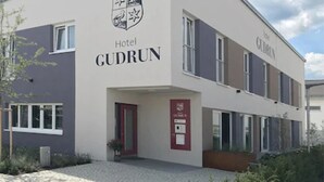 Un moderno edificio de hotel llamado 'Hotel Gudrun', con una entrada despejada, una puerta roja y una señal visible de seguridad contra incendios.