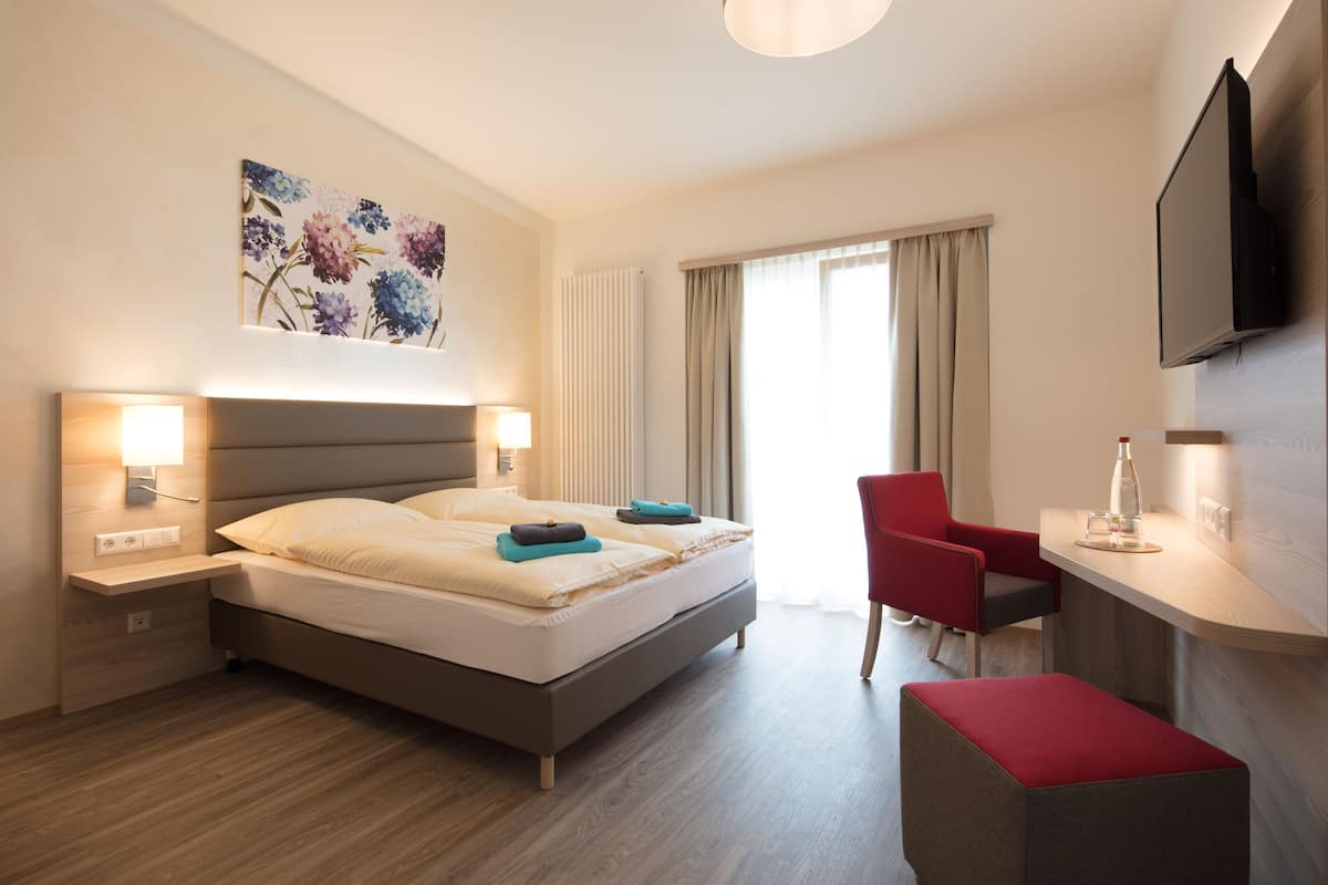 Una habitación de hotel moderna con cama, mesitas de noche, un escritorio, una silla, televisor y ventana con cortinas.