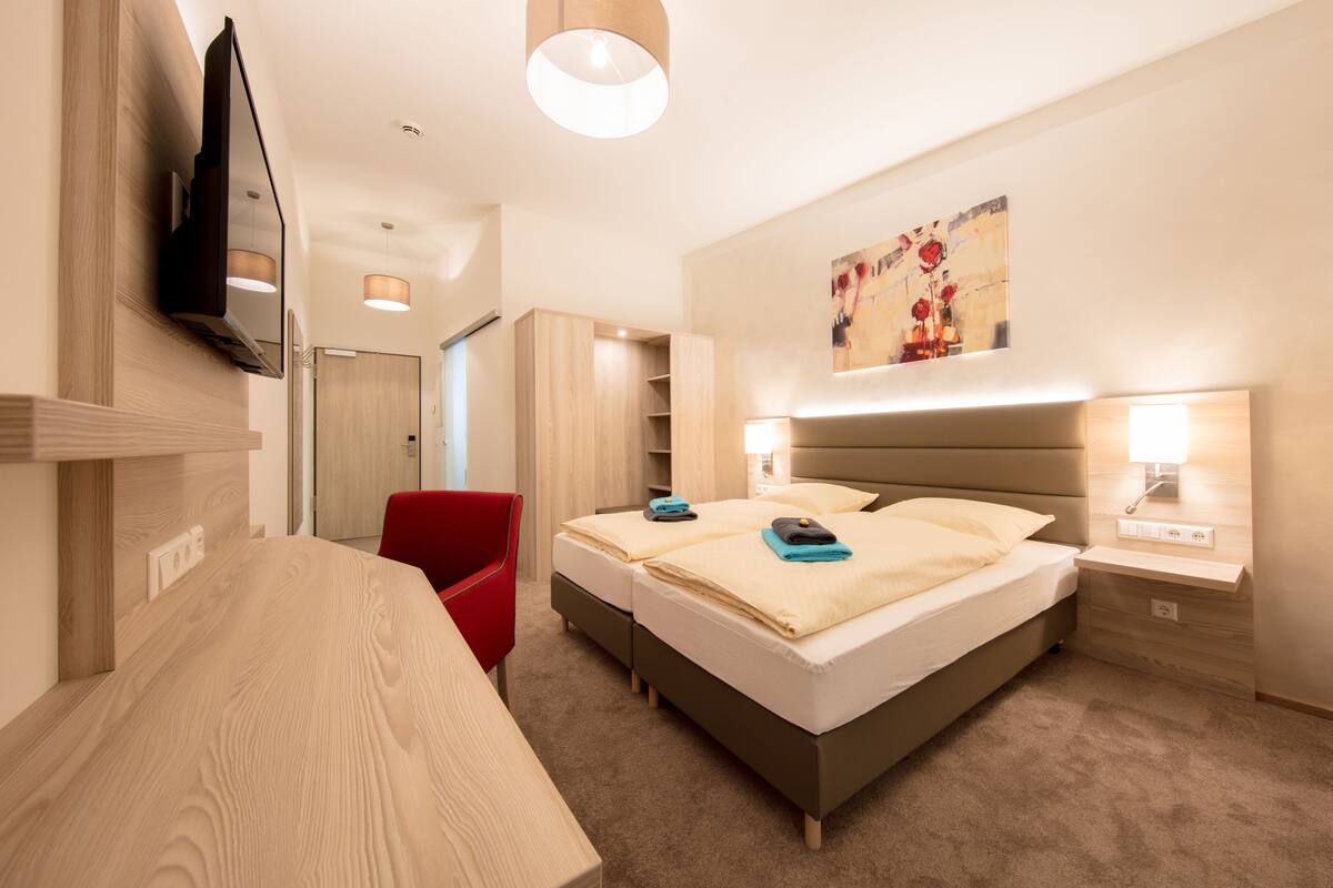 Una habitación de hotel moderna con cama, mesita de noche, televisor y una silla roja.