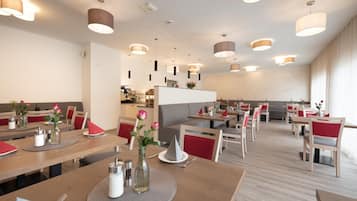Ein modernes Restaurant mit Holztischen, roten Sitzgelegenheiten und Pendelleuchten.