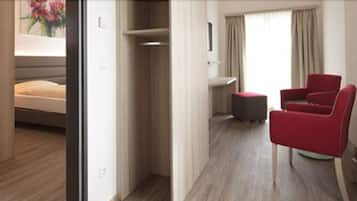 Una habitación de hotel con una cama, un sillón rojo, una mesita y una ventana con cortinas.