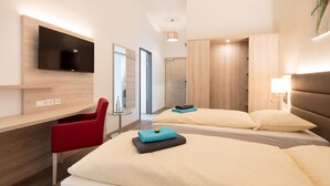 Una habitación de hotel moderna con un televisor de pantalla plana grande montado en la pared, una silla roja, dos camas con ropa de cama color beige y un armario de madera.