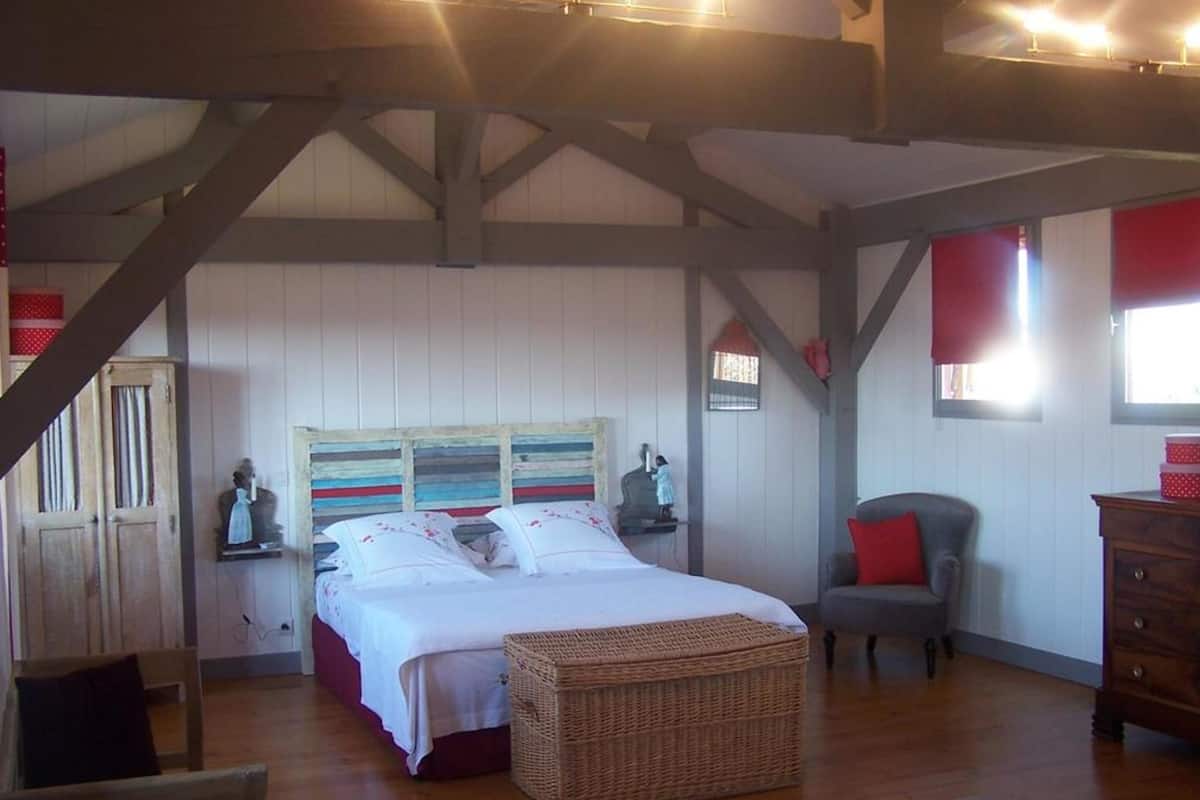 Een slaapkamer met een bed, een stoel, een kast en een raam met rode gordijnen.